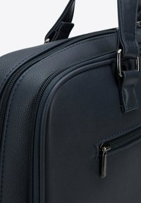 Donkerblauwe leren tas met een gestructureerde afwerking, dubbele ritsen en een voorvak met zilverkleurige hardware. Beschikt over versterkte stiksel details.