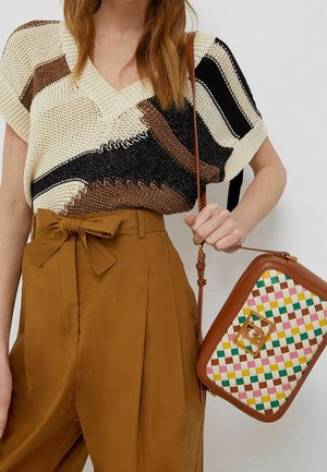 Top en tricot avec des motifs marron, noir et crème, décolleté en V, associé à un pantalon taille haute marron et un sac à main tissé multicolore.