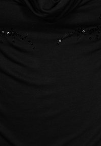 Schwarzes Oberteil aus Stoff mit einem drapierten Ausschnitt, das mit verstreuten schwarzen und silbernen Perlen im oberen Bereich verziert ist. Glatte Textur, lässiges Design.