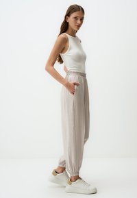 Lichtgrijze wijde broek met een elastische tailleband, zijzakken en geplooide manchetten, gecombineerd met een aansluitend wit tanktop en witte sneakers.