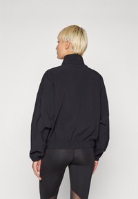 Black cropped jacket with a high collar, long sleeves, and elasticized hem. Smooth, lightweight material with a minimalist design.