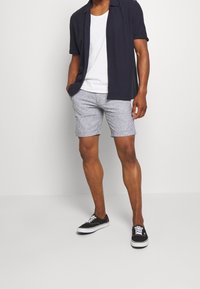 Námořnická košile s krátkým rukávem, bílý top na ramínka, pruhované šortky v modro-bílé barvě a černé tenisky s bílou podrážkou. Neformální letní oblečení.