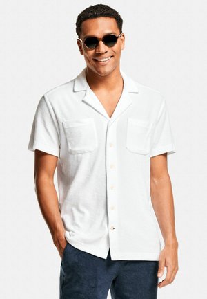 Chemise blanche à manches courtes en tissu éponge, dotée de deux poches avant, d'une fermeture à boutons sur le devant et d'un col décontracté.