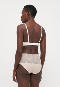 Sostituto bianco con spalline regolabili e chiusura a gancio; abbinato a mutandine rosa chiaro con una vita in pizzo dallo schema a onda.