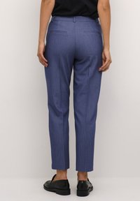 Modré tailorované kalhoty s vláknem odolným proti mačkání, slim-fit střih a dvě zadní kapsy. Nosené s černými plochými botami.