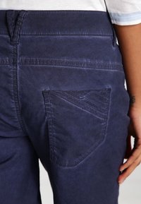 Navyblauwe taps toelopende broek met een achterzak met een diagonaal ontwerp en textuursteken. Glad stof met een lichte glans en schone naden.