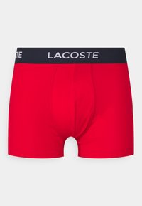 Rdeče bokserice iz elastičnega bombaža, s temnim pasom v mornarsko modri barvi in belim logotipom "LACOSTE". Gladka tekstura in dobro prileganje.