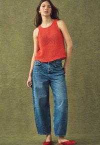 Rød strikket tanktop, høj talje blå jeans og røde flade sko. Løs pasform, struktureret stof og bred ben design. Enkle sølv smykke accenter.