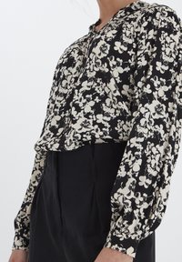 Černá blůza s bílým květinovým vzorem; lehká tkanina, dlouhé nafouknuté rukávy, design na knoflíky vpředu a uvolněný střih.