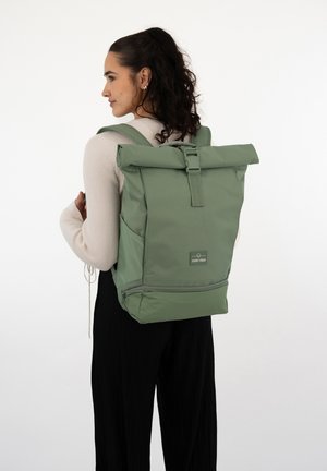 Rucsac cu capac rabatabil în verde mat, realizat dintr-un material durabil. Include curele ajustabile, o petică cu logo în față și buzunare laterale.