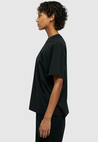 T-shirt en coton noir avec une coupe décontractée, des manches courtes et un col rond. Présente un design simple sans motifs ni embellissements visibles.