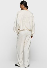 Sweatshirt oversize couleur crème et pantalon assorti, avec logo brodé au dos, fabriqués en tissu doux avec une coupe décontractée.