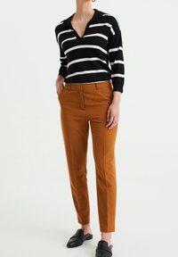 Pruhovaná pletená polo košile v černobílé barvě s límcem, spárovaná s úzkými kalhotami v rezavé barvě a černými botami na slip-on.