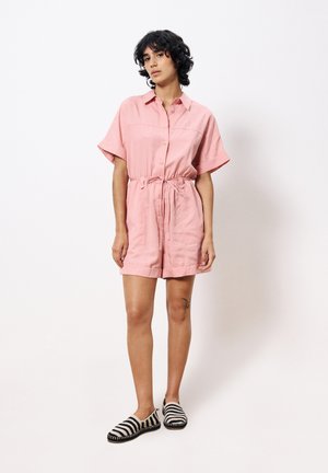 Combi-short rose à manches courtes avec fermeture à boutons et taille à cordon, associé à des chaussures à enfiler noir et blanc à rayures, tissu lisse, coupe décontractée.