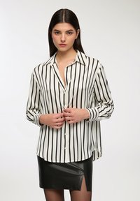 Camicia button-up a righe bianche e nere con maniche lunghe, dotata di colletto classico e dettagli con bottoni, abbinata a una gonna in pelle nera.