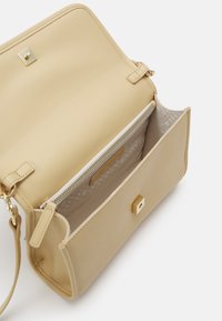 Sac bandoulière beige avec rabat ouvert montrant un compartiment intérieur zippé et une doublure en tissu avec un motif subtil.
