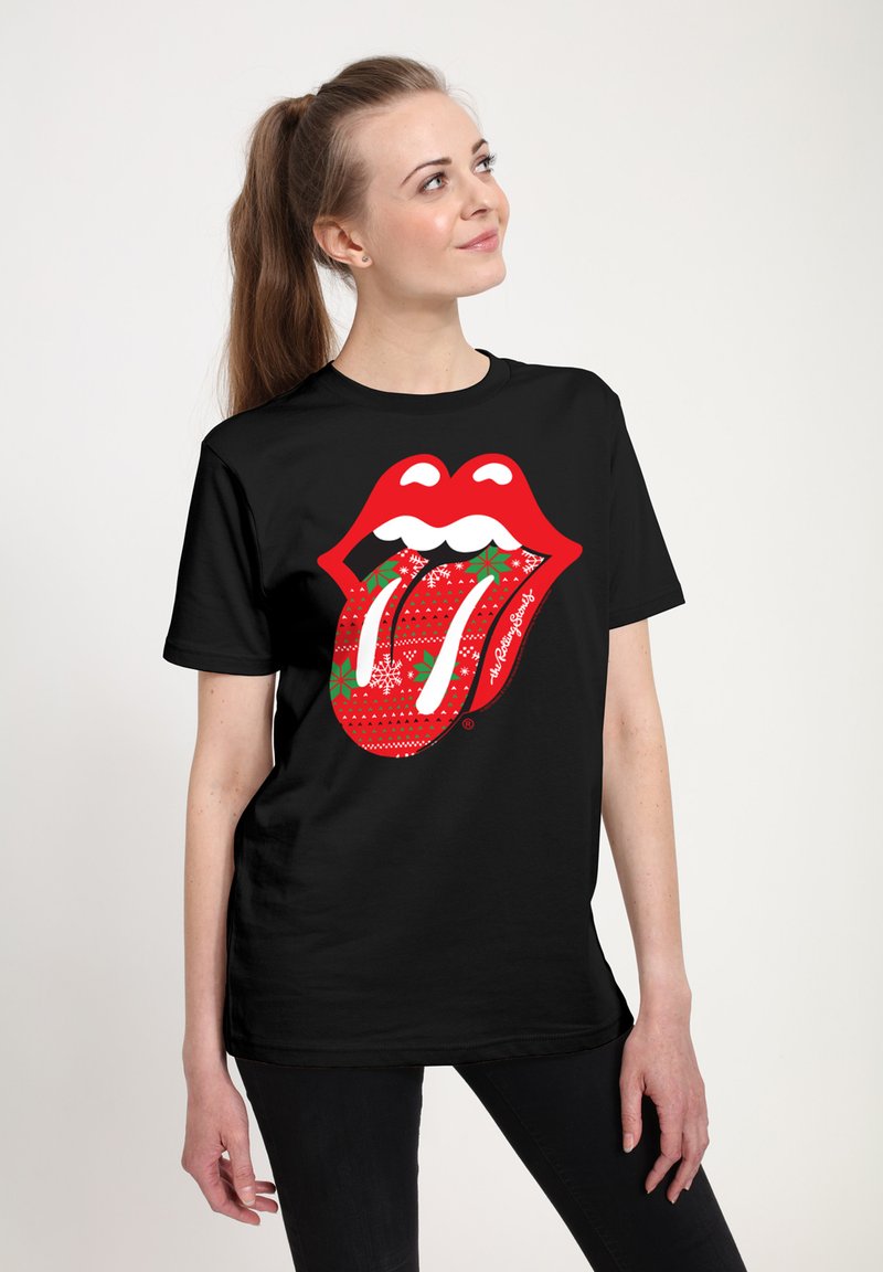 Woman with long brown hair in a ponytail wearing a black t-shirt with a red Rolling Stones tongue logo decorated with Christmas patterns.