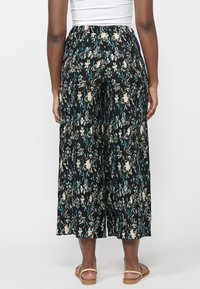 Kvetinové culottes v čiernej farbe, s plisovaním, širokými nohavicami a elastickým pásom pre pohodlie. Obuv na podpätku dopĺňa vzhľad.
