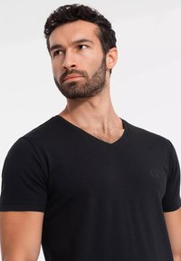 Czarny t-shirt z dekoltem w serek, wykonany z miękkiego materiału, z krótkimi rękawami i subtelnym haftowanym logo po lewej stronie klatki piersiowej.