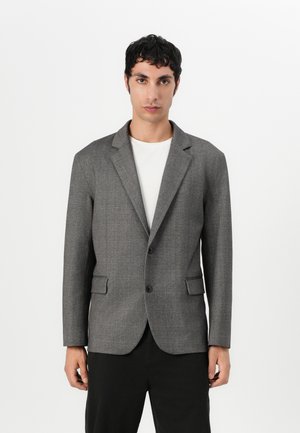 Grauer Blazer aus strukturiertem Stoff, mit Reverskragen, Ein-Knopf-Verschluss und zwei vorderen Taschen, getragen über einem weißen Hemd.