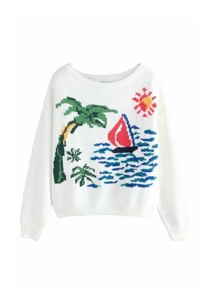 Kvinde stående ved vandet iført en sweater med et motiv af en sejlbåd og et palmetræ samt blåternet shorts under en klar himmel.