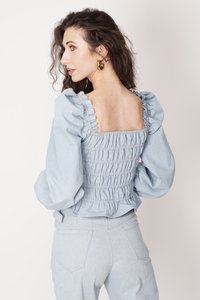 Jasnoniebieska bluzka z puffowanymi rękawami i kwadratowym tyłem, z marszczonymi detalami i miękką teksturą. Połączona z jasnobłękitnymi spodniami z wysokim stanem.