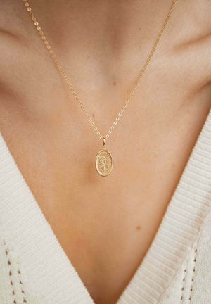 Gold pendant necklace featuring an oval charm with an embossed floral design, hanging from a delicate chain against a light sweater.
