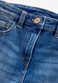 Denim jeans in een donkerblauwe tint. Kenmerken zijn onder andere een messing knoopsluiting, stevige stiksels en een gladde textuur met subtiele vervaging.
