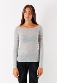 Maglietta a maniche lunghe grigia chiara a costine con scollatura ampia, caratterizzata da un design aderente e una texture morbida, abbinata a pantaloni neri a righe sottili.