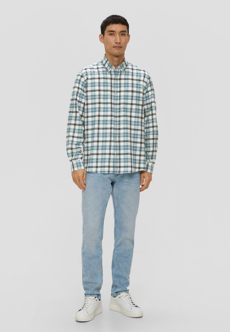 Chemise à carreaux en bleu, vert et blanc, avec un col boutonné et des manches longues. Portée avec un jean bleu clair et des baskets blanches.