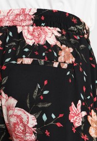 Elastisk midjeband med svarta byxor i tyg som har ett blommönster av rosa, orange och röda blommor med gröna blad och en fickdetalj.