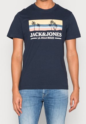 Granatowy T-shirt z grafiką palmy i napisem "JACK & JONES LA JOLLA BEACH" noszony przez osobę w jasnoniebieskich dżinsach.