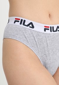 Slip in cotone grigio con cinturino elastico bianco che presenta il logo FILA in nero e rosso. Il tessuto è liscio con un design aderente.