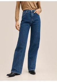 Jeans azules de tiro alto con un corte holgado, hechos de denim. Presentan un diseño tradicional de cinco bolsillos y costuras en contraste. Calzado negro plano.