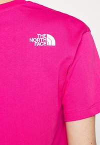 Korte mouw hotpink T-shirt van katoen met een ronde hals en een wit logo van The North Face op de bovenrug. Glad textuur.