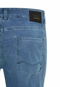 Blaue Jeans aus Denim mit strukturierter Oberfläche, versehen mit einem schwarzen Etikett mit goldenen Buchstaben und zwei Gesäßtaschen mit Ziernähten.