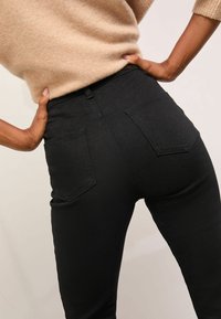 Černé skinny džíny zdenimu s vysokým pasem, které mají dvě zadní kapsy a hladkou texturu. Materiál vypadá elasticky a přiléhavě.