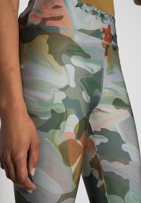 Leggings med ett multikolorert, abstrakt mönster i gröna, bruna och hintar av rosa, tillverkade av mjukt, sträckbart tyg.