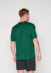 Groene mesh sport t-shirt met korte mouwen, ronde halslijn en zijstrepen. Draagt met zwarte shorts, achteraanzicht toont textuur.
