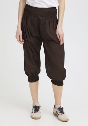 Person wearing black cropped pants with smocked elastic waistband and cuffs, paired with white and black sneakers on a white background.