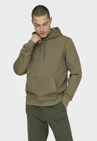 Sudadera color caqui hecha de mezcla de algodón, con capucha ajustable, bolsillo tipo canguro, puños acanalados y un corte relajado. Textura suave.