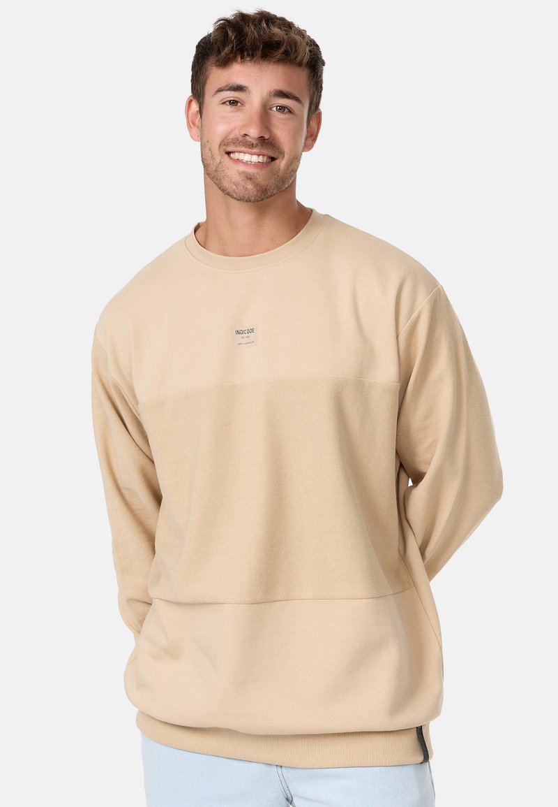 Beżowy długi rękaw sweatshirt z teksturowanym panelem, okrągłym dekoltem i małą naszywką z logo na piersi. Miękki materiał i luźny krój.