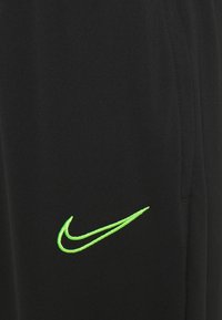 Schwarze Sporthosen mit weicher Textur, die ein auffälliges neon grünes gesticktes Nike-Logo auf der linken Seite aufweisen.