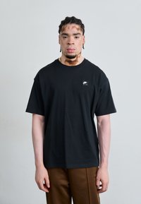 Black cotton t-shirt with a round neckline and short sleeves, featuring a small white Nike logo on the left chest area.