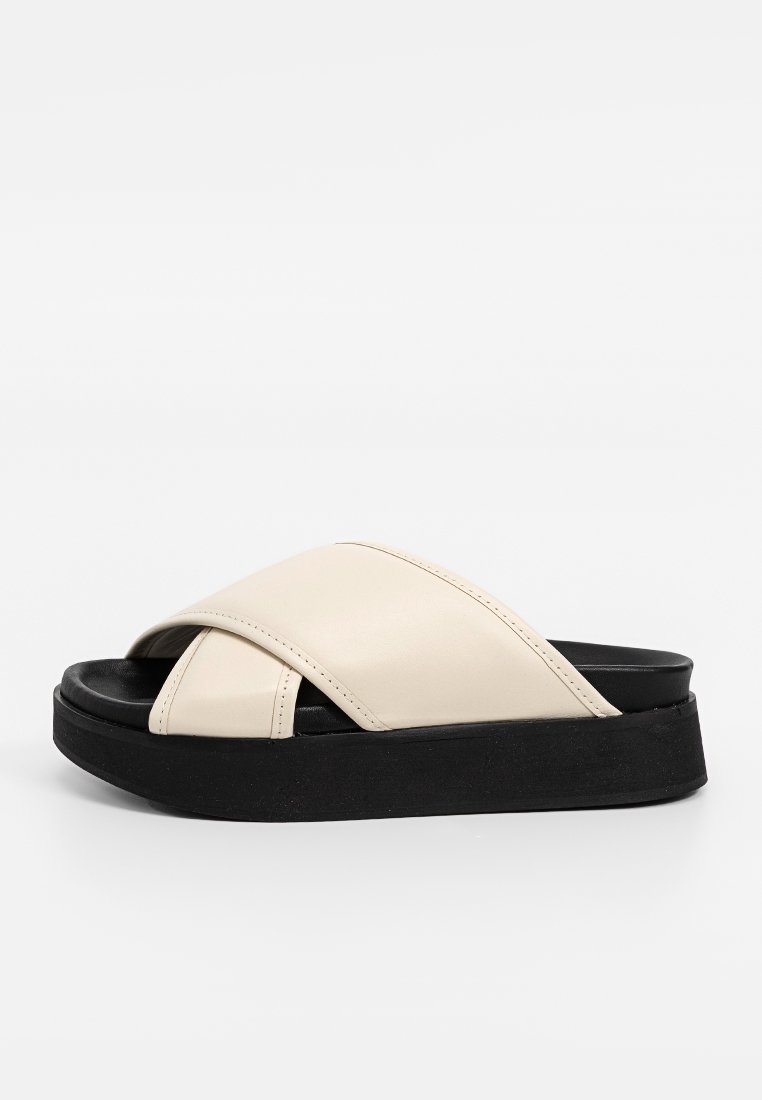 Sandales à glissière croisées en simili cuir crème avec une semelle plate-forme noire texturée et un design à bout ouvert.