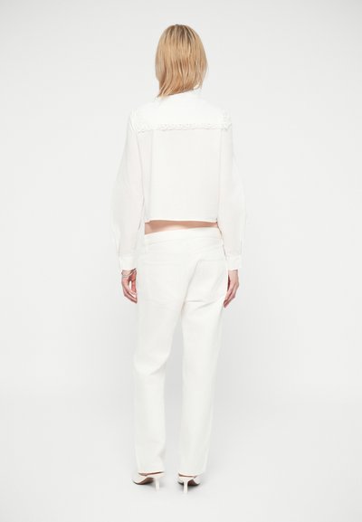 Blouse blanche courte avec des détails en dentelle sur les épaules, associée à un pantalon blanc taille haute. Texture lisse, design minimal et lignes épurées.