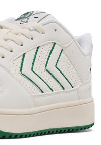 Vit sneaker i texturerat läder, med gröna chevrondetaljer, perforeringar och en tjock vit mellansula med en grön gummisula.