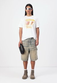 Hvit grafisk t-skjorte med gult og rosa design, lyseblå denimshorts, beige snøresko, og en svart clutchveske.