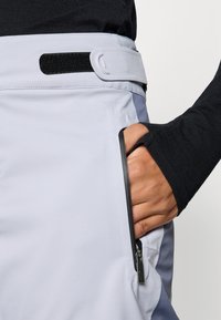 Heledad hallid püksid musta vöökoha ja Velcro sulgemisega; sisaldavad külgpocketit ja sujuvat, pehmet kangast tekstuuri.