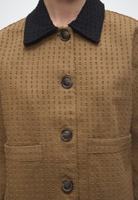 Καφέ υφασμάτινο σακάκι με μεγάλα σκουρόχρωμα κουμπιά, μαύρο υφασμάτινο γιακά και δύο εμπρόσθιες τσέπες.